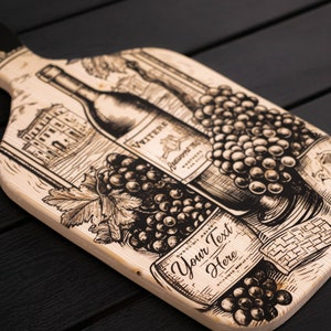 May include: A wooden cutting board with a black and white illustration of wine bottles, grapes, and a building. The text "Your Text Here" is printed on the board.