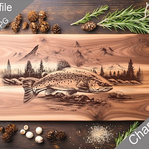 Puede incluir: Una tabla de cortar de madera con un diseño grabado con láser de una trucha saltando de un río con montañas en el fondo. El texto "Charcuterie design" está impreso en la esquina inferior derecha de la tabla.