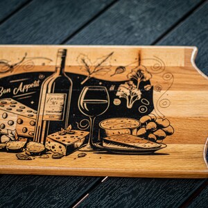 May include: A wooden cutting board with a black and white design of a wine bottle, a glass of wine, cheese, grapes, and the text "Bon Appetit".