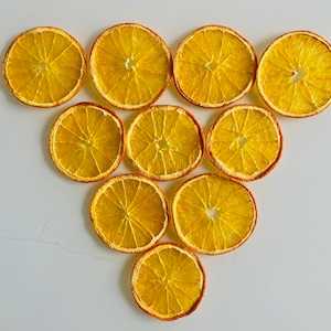 Puede incluir: Diez rodajas de naranja deshidratadas dispuestas en forma triangular. Las rodajas son de un color amarillo-naranja vibrante con un borde naranja más oscuro. La imagen es una vista cenital, mostrando la textura y detalles de la fruta.
