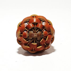 May include: A brown leather button with a gold wire design in the centre. The button has a flower-like shape with multiple layers.