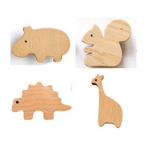 May include: Four wooden animal shapes: a hippo, a squirrel, a dinosaur, and a giraffe. Each is cut from light-colored wood with a smooth finish. The hippo, squirrel, and dinosaur have small black dot eyes. The giraffe has a long neck.