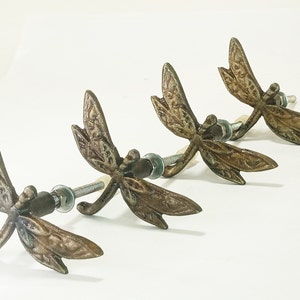 May include: Four antique bronze dragonfly cabinet knobs with a detailed design. Each knob has a screw for attaching to a cabinet door.