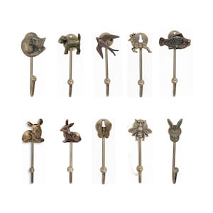 Könnte beinhalten: Eine Sammlung von zehn Wandhaken aus Metall in Bronzetönen. Jeder Haken zeigt ein anderes Tier- oder naturnahes Design, darunter ein Fuchs, ein Hund, ein Vogel, ein Hirsch, ein Fisch, ein Kaninchen, ein Schmetterling, eine Biene und eine Eule. Weißer Hintergrund.