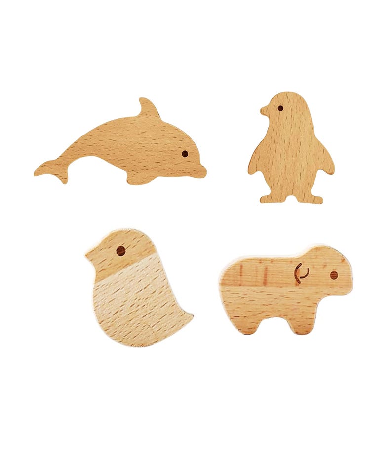May include: Four wooden animal cutouts: a dolphin, a penguin, a bird, and a small mammal. Each cutout is made of light-colored wood with simple, rounded shapes and small, dark dots for eyes. The dolphin is swimming, the penguin is standing, the bird is perched, and the mammal is walking.