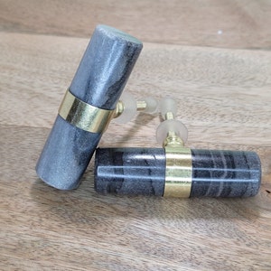 May include: Two grey marble cabinet knobs with gold metal accents. The knobs are cylindrical in shape and have a smooth, polished finish.