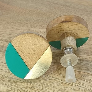 May include: Two wooden cabinet knobs with a geometric design. One knob is green, gold, and brown. The other knob is green and brown. Both knobs have a silver screw.