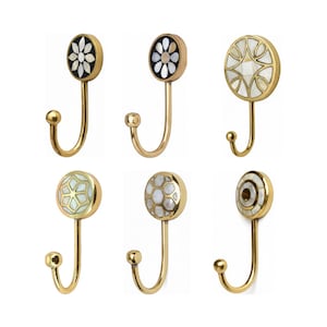Peut inclure: Six crochets décoratifs en laiton avec différents motifs incrustés. Les crochets ont une forme incurvée avec une petite boule à l'extrémité et un dessus décoratif circulaire avec des motifs floraux et géométriques.