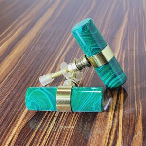 Könnte beinhalten: Zwei grüne und goldene Schrankknöpfe mit einem Malachit-Muster. Die Knöpfe sind aus Naturstein und haben eine Messing-Oberfläche.