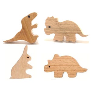 May include: Four wooden toy figures: a Tyrannosaurus Rex, a Triceratops, a rabbit, and a Stegosaurus. Each figure is made of light-colored wood with a smooth finish and small black dot eyes. The toys are designed for children.