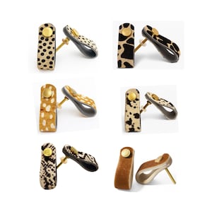 May include: A selection of handcrafted earrings with animal print patterns. Each pair features a rectangular stud with a gold-tone detail and a curved, open-backed dangle. The earrings display designs such as leopard, cow, and snake prints.