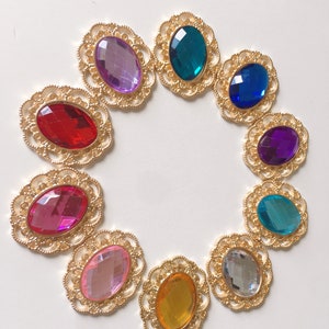 May include: Ten oval gemstones in a variety of colours, including red, purple, and blue, are set in gold-coloured filigree frames. The gemstones are arranged in a circle, creating a decorative display. The frames have an ornate, openwork design.