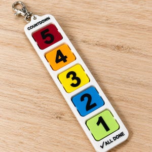 May include: A white plastic countdown keyring featuring five colourful square tiles with black numbers 5, 4, 3, 2, and 1. The top is labelled COUNTDOWN and the bottom reads ALL DONE with a tick. It includes a silver metal lobster clasp.