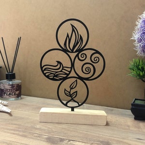 Könnte beinhalten: Schwarze Metallsculptur aus vier Kreisen, die die vier Elemente Feuer, Wasser, Luft und Erde darstellen. Die Skulptur steht auf einem Holzsockel.