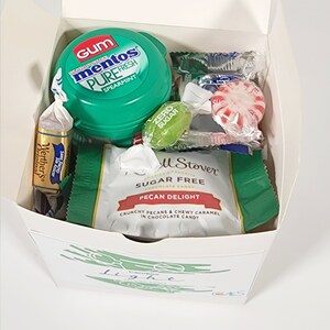 May include: A white gift box filled with assorted candies. The box has a green and white design with the word "Candies" and the word "Light" written in cursive. The candies include a roll of sugar-free pecan delight chocolate candy, a pack of sugar-free Werther's Original candies, a pack of sugar-free Mentos gum, and a few hard candies.