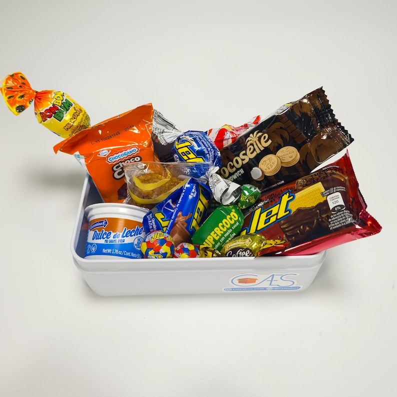 May include: A white rectangular container filled with a variety of colorful candies and snacks. The assortment includes wrapped chocolates, cookies, and hard candies, with packaging in shades of orange, blue, yellow, and red. The container has a logo on the side.