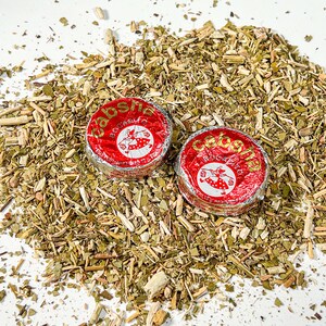 May include: Two red and silver foil-wrapped packages of yerba mate tea, labelled "Caba&ntilde;a", on a bed of loose dried yerba mate leaves.