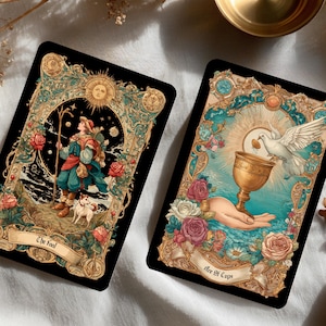 Puede incluir: Dos cartas de tarot con dise&ntilde;os ornamentados. Una carta presenta una figura con un bast&oacute;n y un perro, etiquetada como "The Fool". La otra muestra una mano sosteniendo un c&aacute;liz con una paloma, etiquetada como "Ace of Cups". Ambas cartas tienen motivos florales y celestiales.