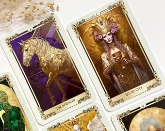 Könnte beinhalten: Ein Satz Tarotkarten mit goldenen Akzenten und Illustrationen von Menschen und Tieren. Die Karten tragen die Namen "The Lovers", "The Strength", "Ace of Cups" und "The World".