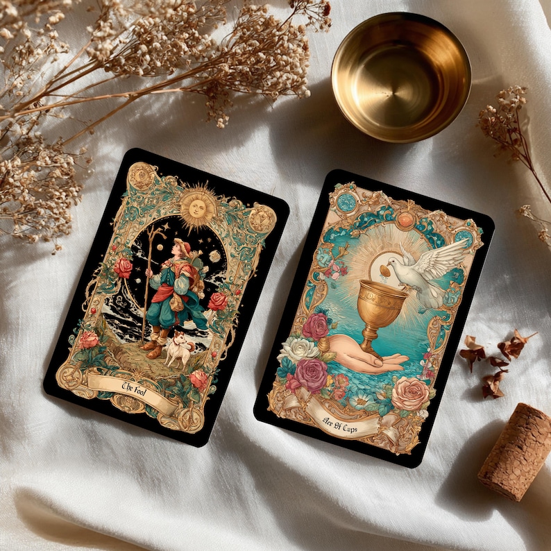 Puede incluir: Dos cartas de tarot con dise&ntilde;os ornamentados. Una carta presenta una figura con un bast&oacute;n y un perro, etiquetada como "The Fool". La otra muestra una mano sosteniendo un c&aacute;liz con una paloma, etiquetada como "Ace of Cups". Ambas cartas tienen motivos florales y celestiales.