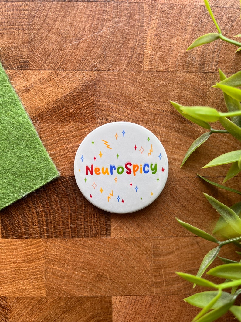 May include: White round sticker with the text "NeuroSpicy" in colorful letters. The sticker is decorated with colorful stars and lightning bolts.