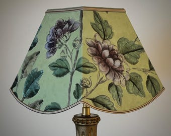 May include: A decorative lampshade with a floral design. The lampshade features a light green and yellow background with purple and green floral illustrations. The lampshade is placed on a gold-colored lamp base.
