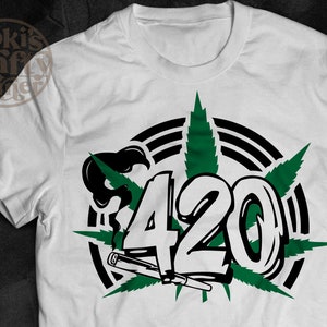 Pode incluir: Camiseta branca com um design de folha de marijuana verde e o número 420 em preto e branco. O design é rodeado por um círculo preto e branco com listras.