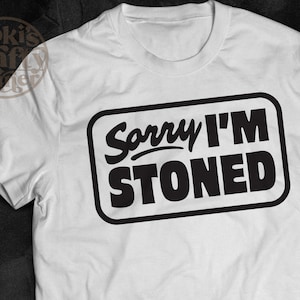May include: White t-shirt with a black rectangle containing the text "Sorry I'm Stoned".