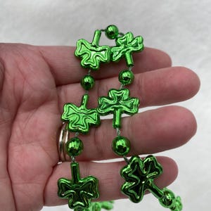 May include: A green shamrock beaded garland with metallic green shamrock charms. The garland is strung on a thin green string.