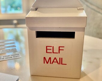 May include: White wooden mailbox with a red "ELF MAIL" label. The mailbox has a slot for letters and a hinged lid.