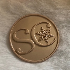 May include: A gold-colored metal charm with the letters "SC" and a snowflake design.