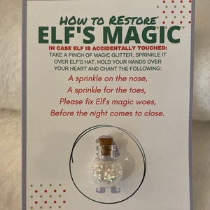 May include: A white card with green and red polka dots. The card has the text "How to Restore Elf's Magic" in green and red letters. The text continues with instructions on how to restore an elf's magic. The card also has a small, clear bottle with a cork stopper and white glitter inside.