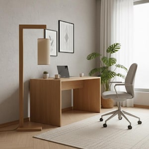 May include: A contemporary home office with a light wood desk, a grey office chair, and a floor lamp with a beige lampshade. A laptop and two framed artworks are on the wall. A potted plant and a patterned rug complete the space.