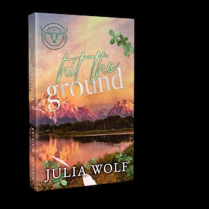 May include: A book cover with a scenic landscape featuring mountains, a lake, and a sunset. The title "hit the ground" is in green script, with the author's name, Julia Wolf, at the bottom. A logo with a bull is at the top.