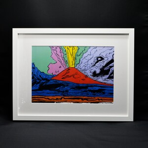Puede incluir: Una impresión enmarcada de una pintura abstracta colorida que representa un volcán en erupción con colores amarillos, rojos, azules y verdes. El volcán está rodeado de nubes y humo.