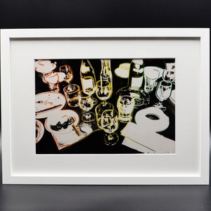 Puede incluir: Una impresión enmarcada de arte pop que representa un servicio de mesa. La obra de arte utiliza una paleta de colores de alto contraste de negro, blanco y amarillo para representar vasos, platos y botellas. La impresión está encerrada en un marco blanco.