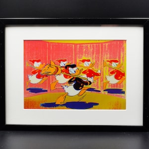 Puede incluir: Una impresión enmarcada de una imagen de dibujos animados de Donald Duck y otros patos en una habitación amarilla y roja. Donald Duck sostiene una escoba y está en primer plano. Los otros patos están en el fondo.