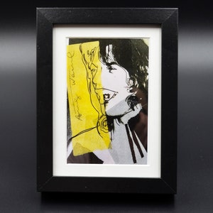 Puede incluir: Un retrato en blanco y negro de una persona con un fondo amarillo. La cara de la persona está parcialmente oscurecida por un trozo de papel amarillo con el texto "Andy Warhol" escrito en él.