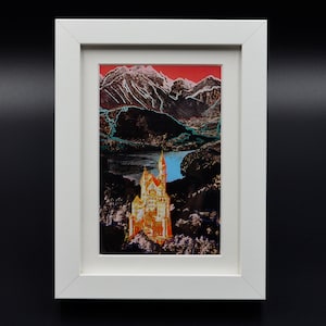 Puede incluir: Una impresión enmarcada de un castillo amarillo en un paisaje montañoso. Las montañas son de color azul oscuro y morado con un cielo rojo y rosa. El castillo está rodeado de árboles y un lago.
