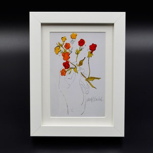 Puede incluir: Una impresión enmarcada de una mano sosteniendo un ramo de flores naranja, rojo y amarillo. La impresión está firmada "Andy Warhol".