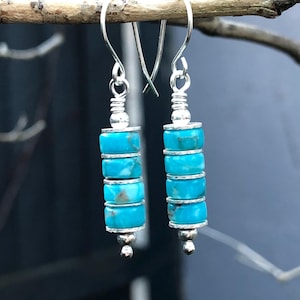 May include: A pair of drop earrings featuring four stacked turquoise-coloured disc beads separated by thin silver-toned metal spacers. The earrings hang from silver-toned ear wires and are finished with a small silver-toned bead at the bottom.