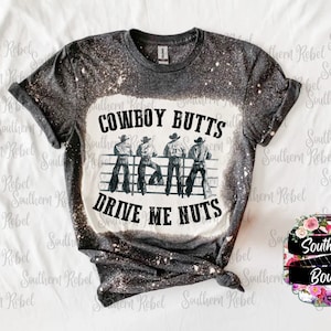 May include: A gray t-shirt with a bleach-splattered design. The shirt features a graphic of four cowboys with the text "COWBOY BUTTS DRIVE ME NUTS".