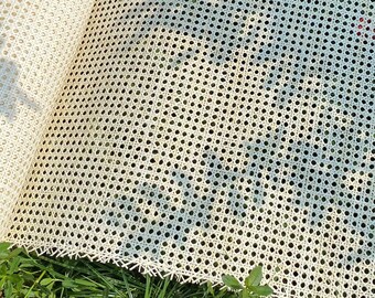 Könnte beinhalten: Eine Rolle weißer Rohrgeflechts, auch bekannt als Caning, liegt auf grünem Gras. Das Geflecht ist ein gewebtes Material, das für Stuhlsitze und -lehnen verwendet wird. Ein Strohhut mit rotem Besatz liegt auf dem Geflecht.