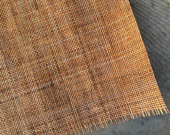 May include: A close-up of a woven cane or bamboo material. The material is light brown in color and has a natural, rustic look. The weave is tight and uniform, creating a smooth surface.
