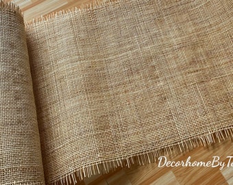 May include: A roll of natural burlap fabric with frayed edges. The fabric is a light brown color and has a woven texture.