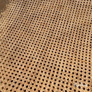 May include: Close-up of a woven cane webbing with a repeating pattern of small, evenly spaced holes. The natural-colored material is tightly woven, creating a textured surface. The webbing is likely used for furniture or decorative purposes.