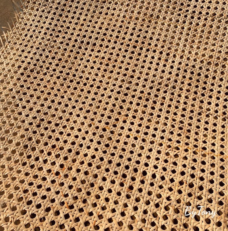 May include: Close-up of a woven cane webbing with a repeating pattern of small, evenly spaced holes. The natural-colored material is tightly woven, creating a textured surface. The webbing is likely used for furniture or decorative purposes.