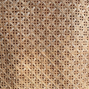 May include: Close-up of a woven cane or rattan material with a diamond pattern. The material is light brown and has a natural, rustic look.