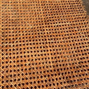 May include: Close-up of a woven rattan material with a repeating pattern of small squares and diamond shapes. The natural-toned material is a light brown colour, with dark shadows creating depth. The texture is visible.