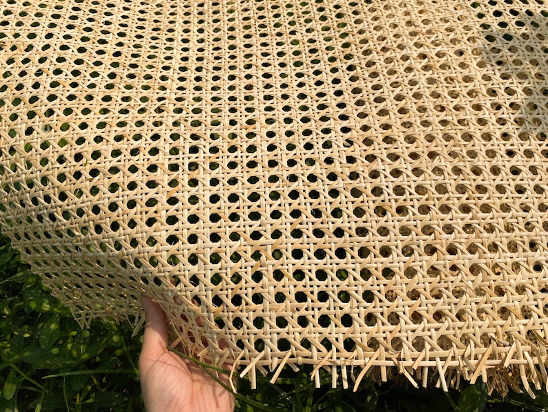 May include: Close-up of a sheet of natural woven cane webbing. The webbing has a repeating pattern of small, evenly spaced holes. The material is a light tan color and appears to be flexible. The edges of the webbing are slightly frayed.